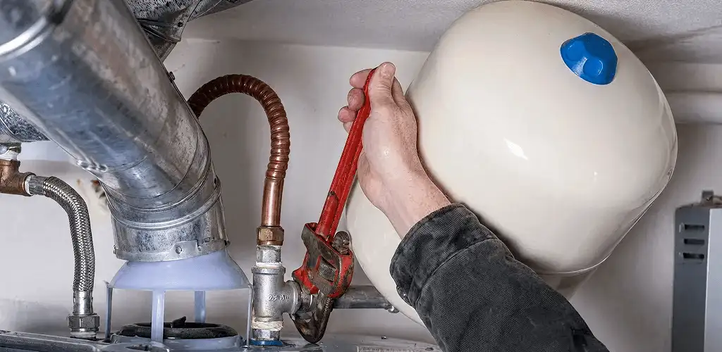 Water heater repair technician tightening plumbing connections near a tank unit in Los Angeles, CA